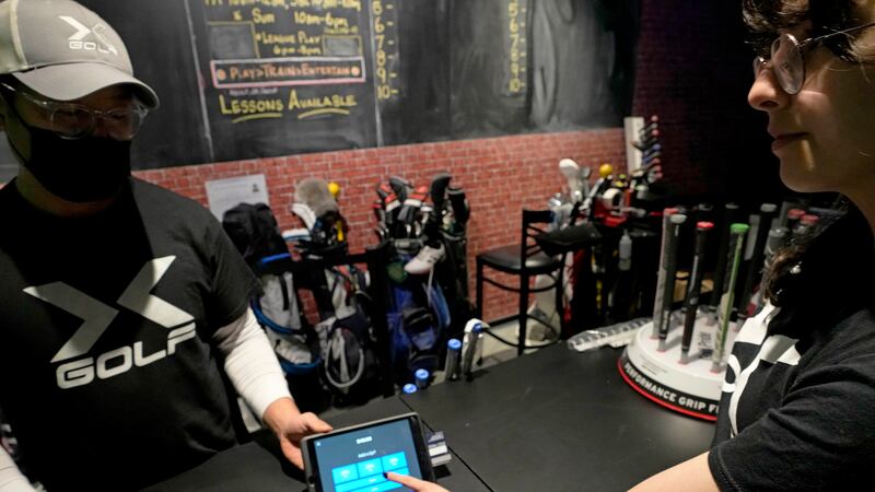 X-Golf manager J.W. Park, left, helps Ashley Moreno to check out at X-Golf indoor golf in...